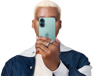 Billedet viser en mand med lys kort hår, iført en hvid og blå jakke, hvor han holder en iPhone 16 med bagsiden af kamerasystemet oppe foran hans hoved