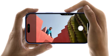 To hænder der holder en iPhone 16 vandret i hver deres ende, mobilens skærm er inde på kameraret, hvor man kan se en mand læne sig over solbrændte murer, hvor manden kigger ud over murene foran ham, i højre hjørne kan man se en kaktus stikke frem