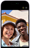 To personer tager en selfie udendørs i solskinsvejr, den ene har en beige hat på.