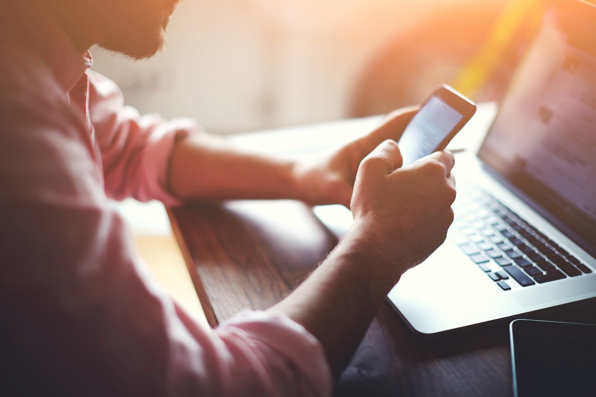 mand bruger mobil og laptop